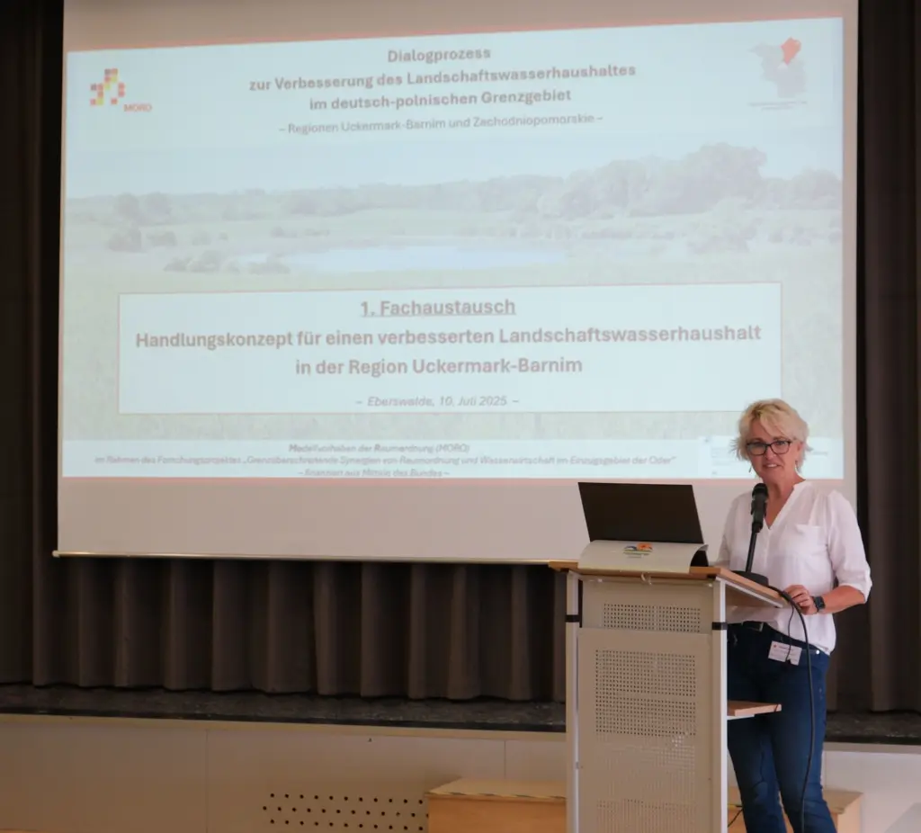 Eine Frau vor einer Leinwand, auf der eine Präsentation abgespielt wird.