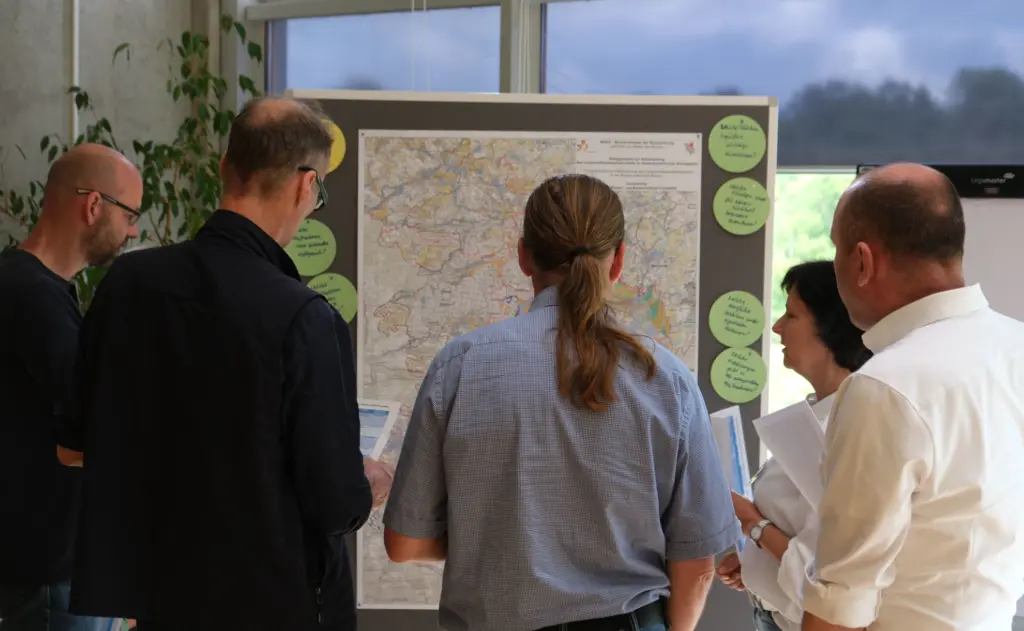 Vier Männer und eine Frau in einer Reihe, mit dem Gesicht zu einer Pinnwand. Auf der Pinnwand ist eine große Karte mit einem Auschnitt der Region Uckermark-Barnim abgebildet. Auf der Karte wurden Klebezettel angebracht mit Hinweisen zu bestimmten Orten auf der Karte.
