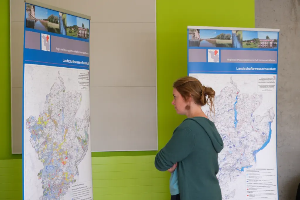 Eine Frau steht vor einem Roll-Up, auf dem eine Karte der Region Uckermark-Barnim abgebildet ist. Im Hintergrund steht ein weiteres Roll-Up.